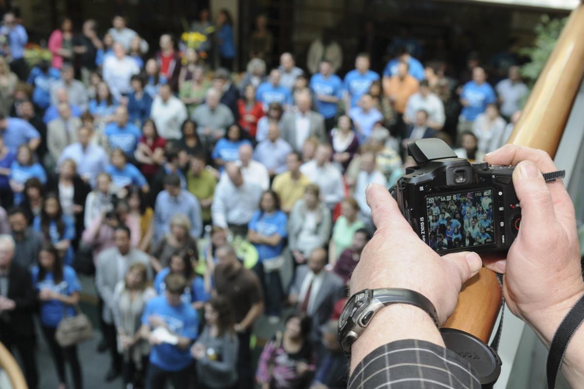 A man takes a picture of a crowd from a balcony.