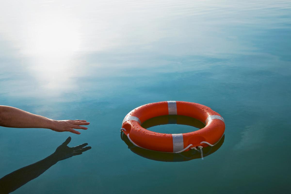A hand reaching for a lifesaver floating on water.