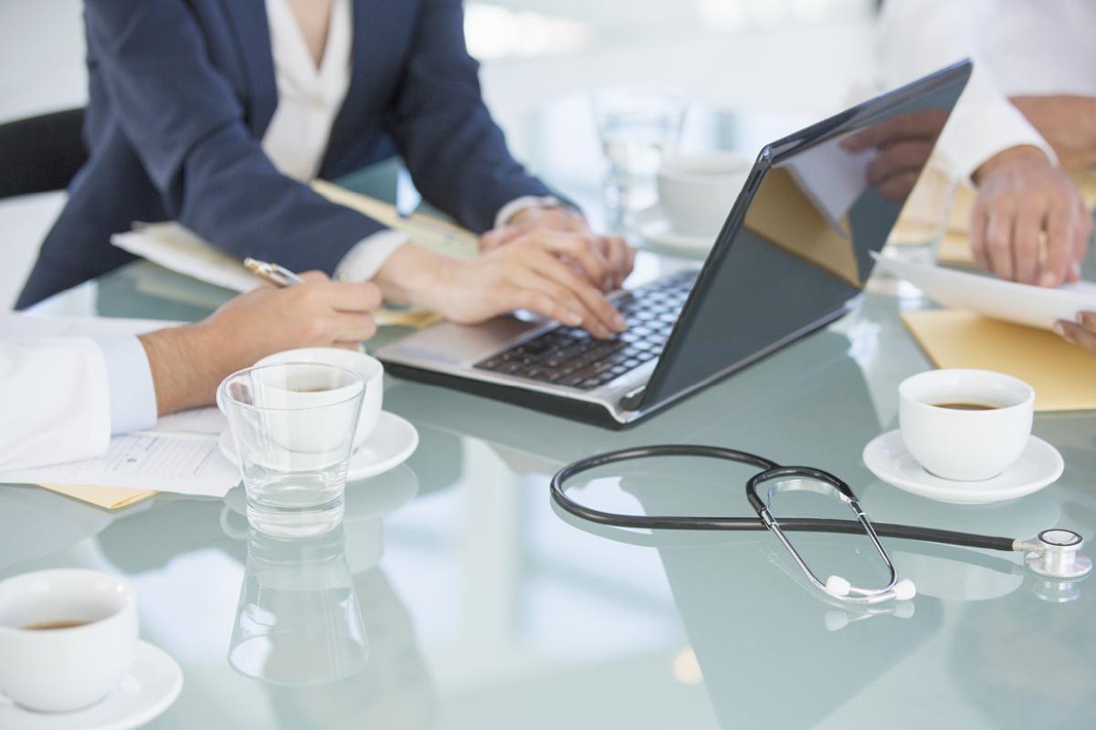 A group of medical professionals having coffee and a discussion while a woman types on a laptop.