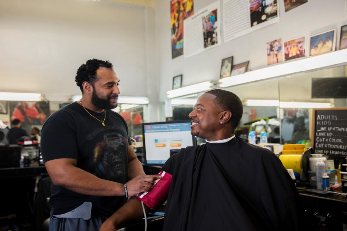 Barber Eric Muhammad places a cuff on Mark Sims to measure his blood pressure at barber shop.