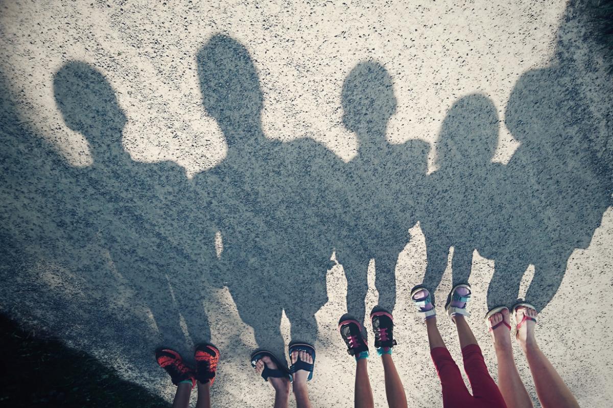 A group of five children look at their shadow against a blacktop.