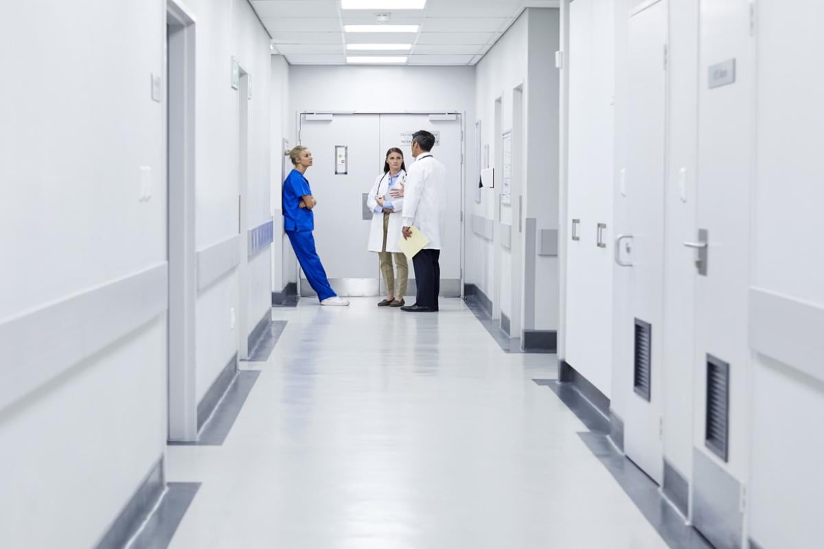 A nurse and two doctors talk in an empty white hallway.