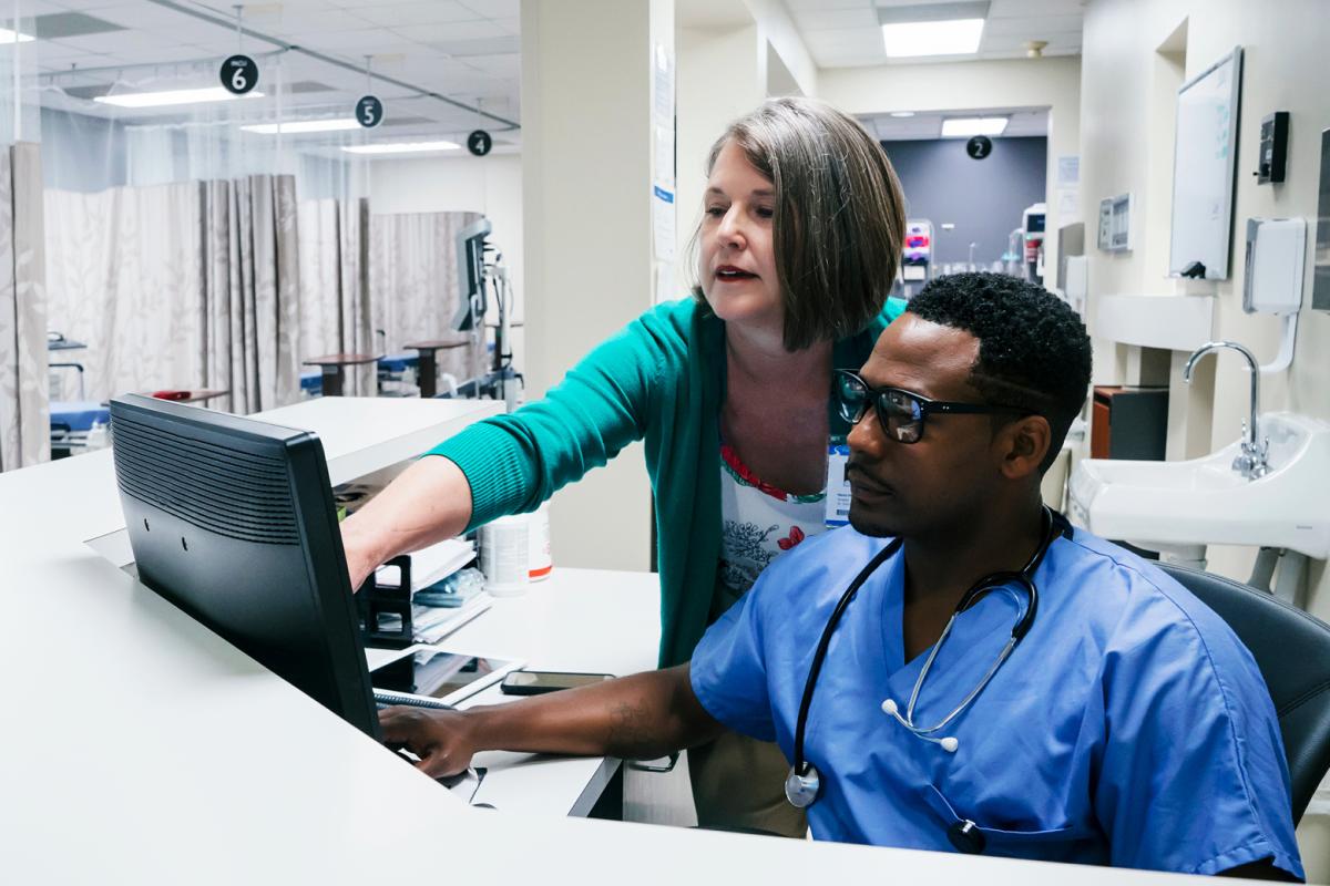A woman shows an African-American male doctor something on a computer screen.
