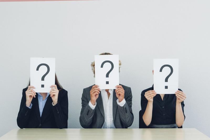 Three people hold a question mark in front of their face